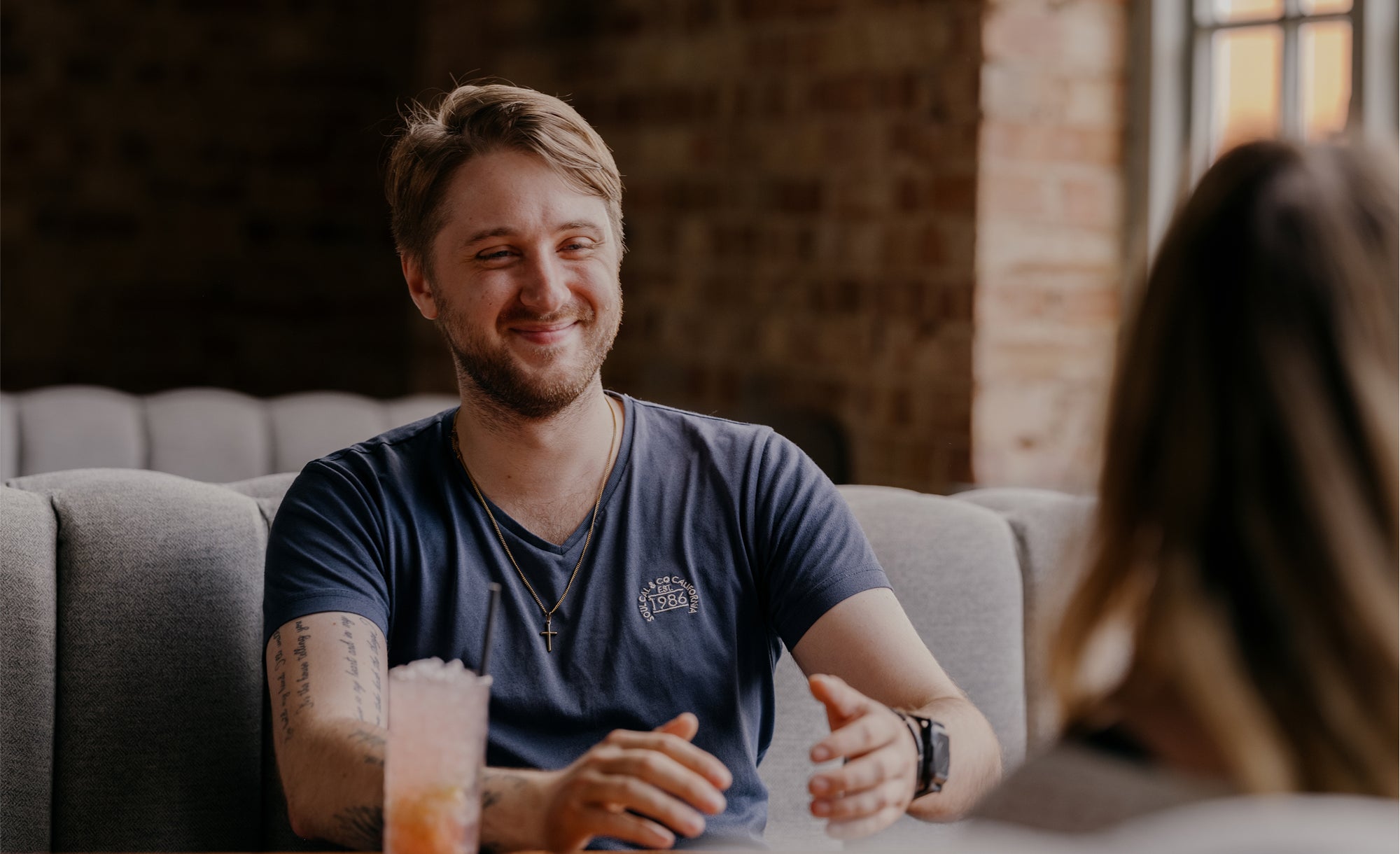 Man sitting on a couch smiling at another person with a blurred background