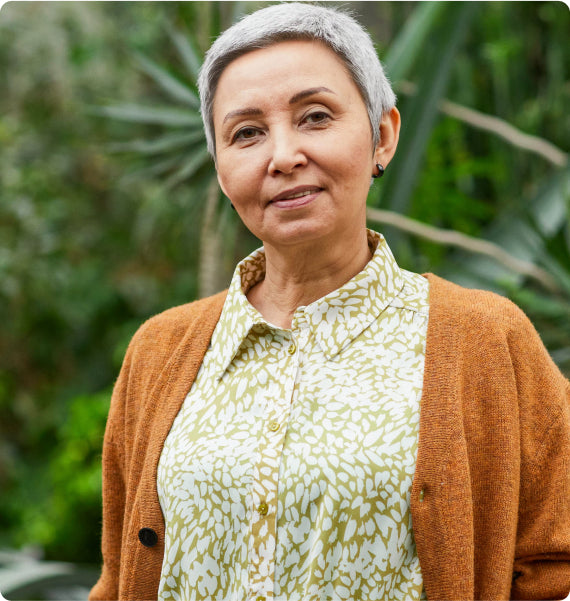 Woman wearing a brown cardigan over a patterned shirt with a blurred green background