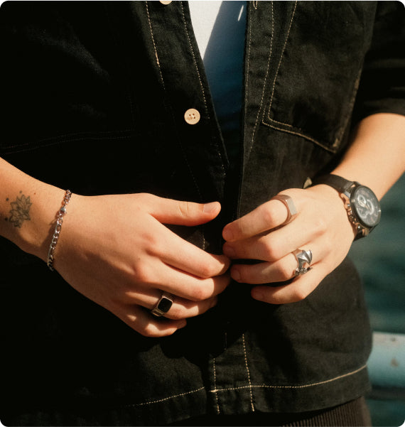 Close-up of hands buttoning a black jacket with jewelry on.